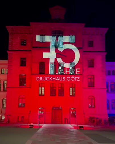Rot angestrahlte Fassade mit der Projektion 75 Jahre Druckhaus Götz